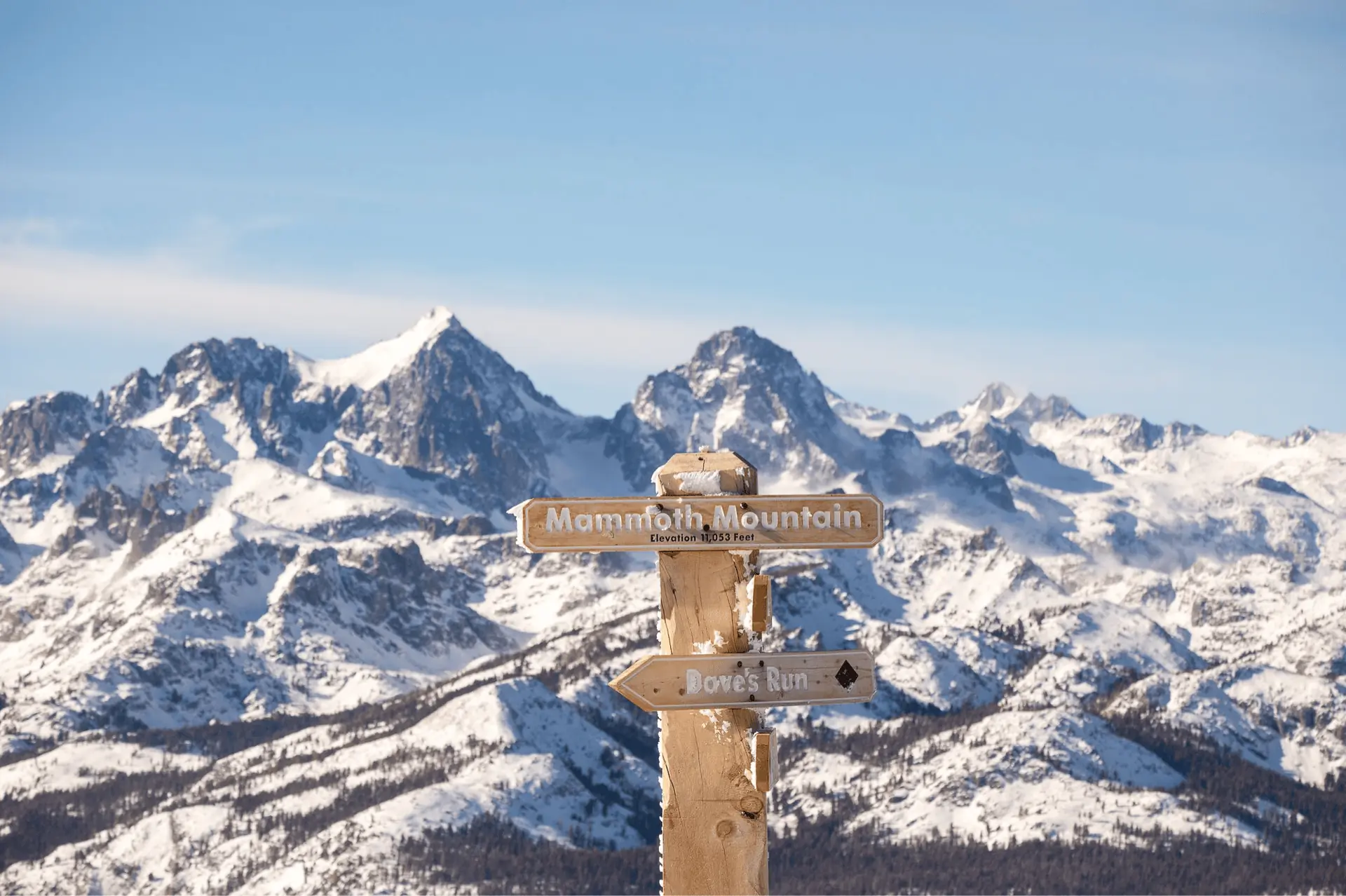 A photograph showing the Mammoth Mountain sign with the Ritter and Banner peaks in the distance.