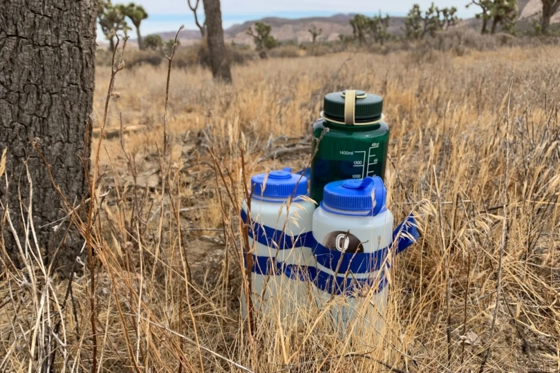 Plastic water bottles and storage containers placed discreetly in the desert brush for a backcountry hike.