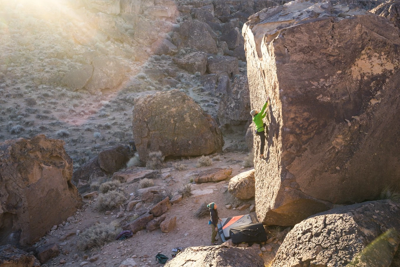 A climber high off the ground on a boulder in Bishop, California, with chalked hands.