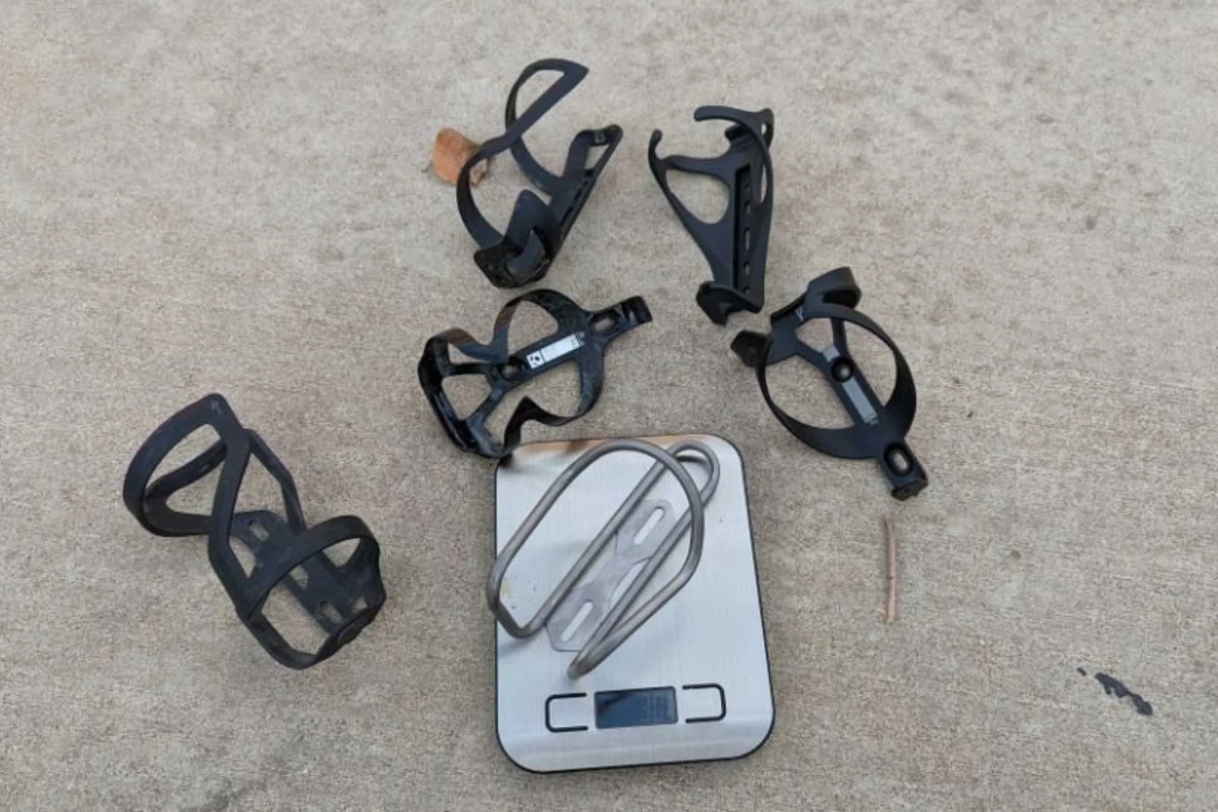 Two water bottle cages being weighed on a precision digital scale side-by-side.