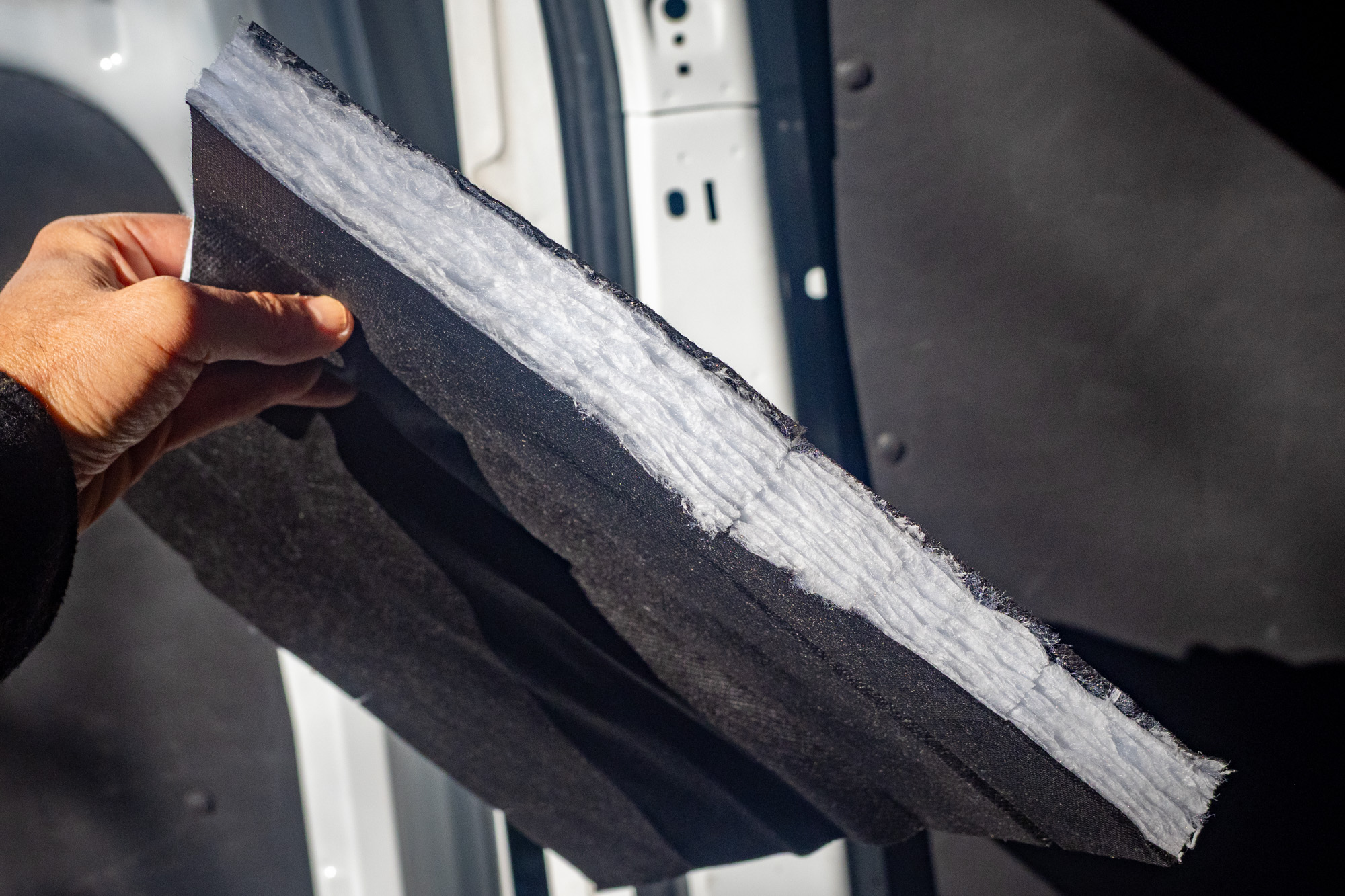 A precut 3M Thinsulate insulation panel being held up against a van wall.