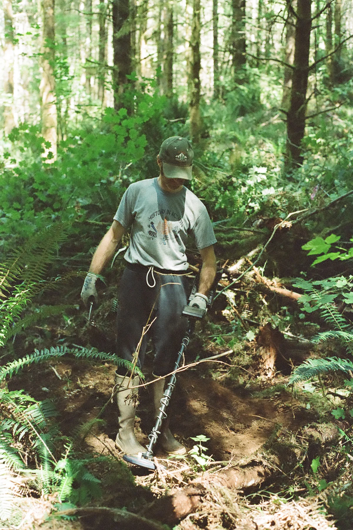 A person using a metal detector in a wooded area to locate buried metallic debris.