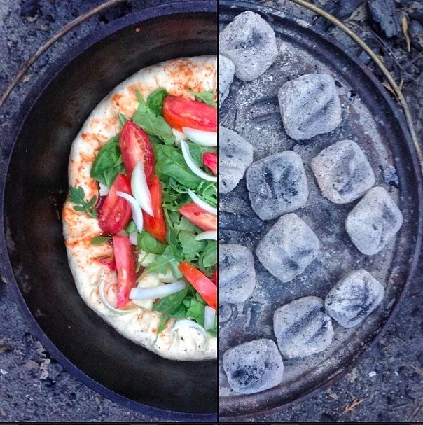A freshly baked pizza inside a cast iron dutch oven at a campsite.