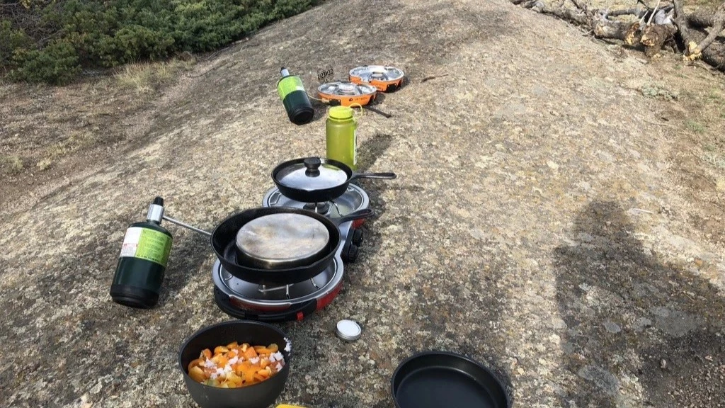 Two green foldable two-burner camping stoves set up on a picnic table.