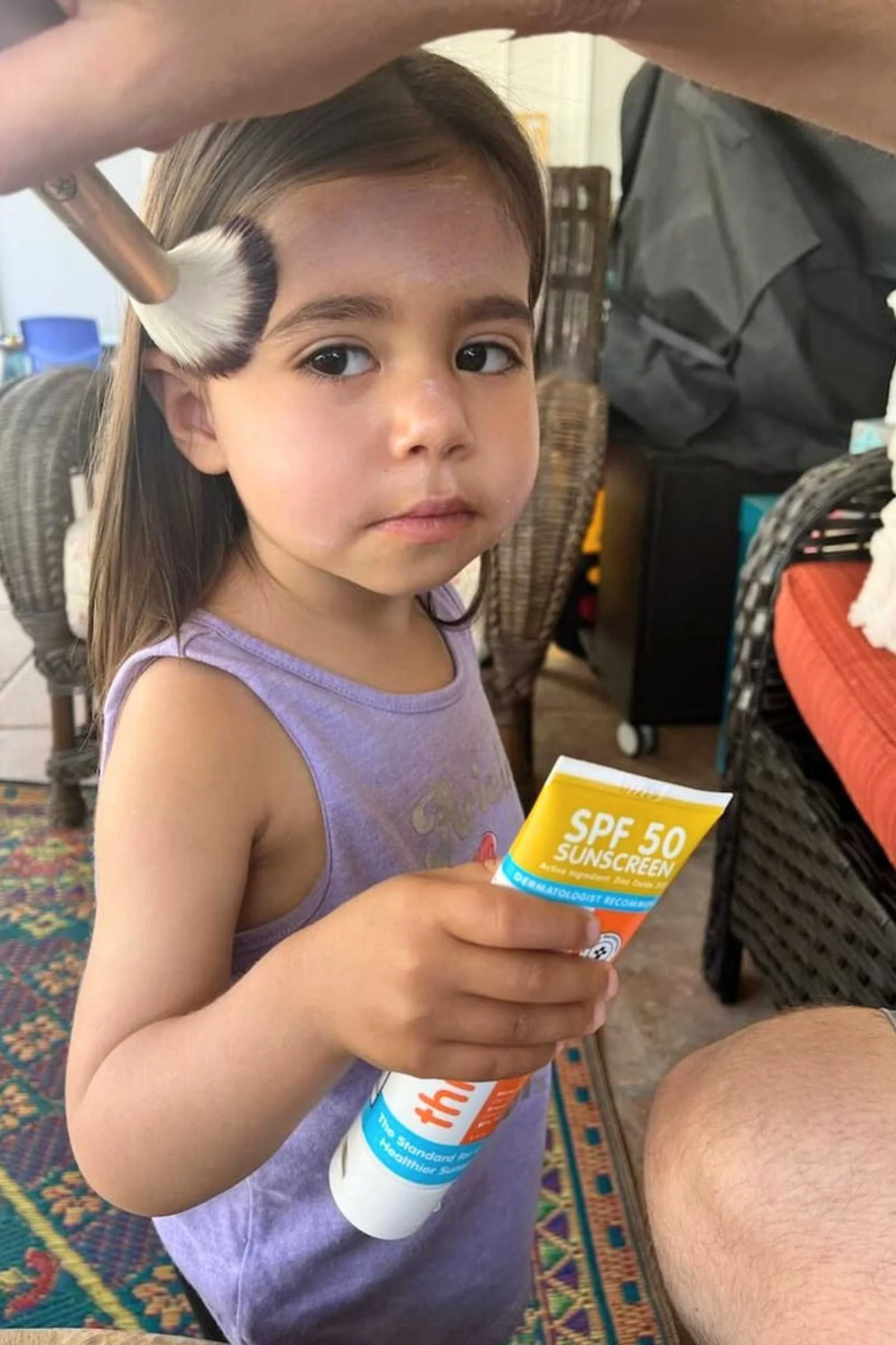 A makeup brush being used to apply mineral sunscreen to a child's face.