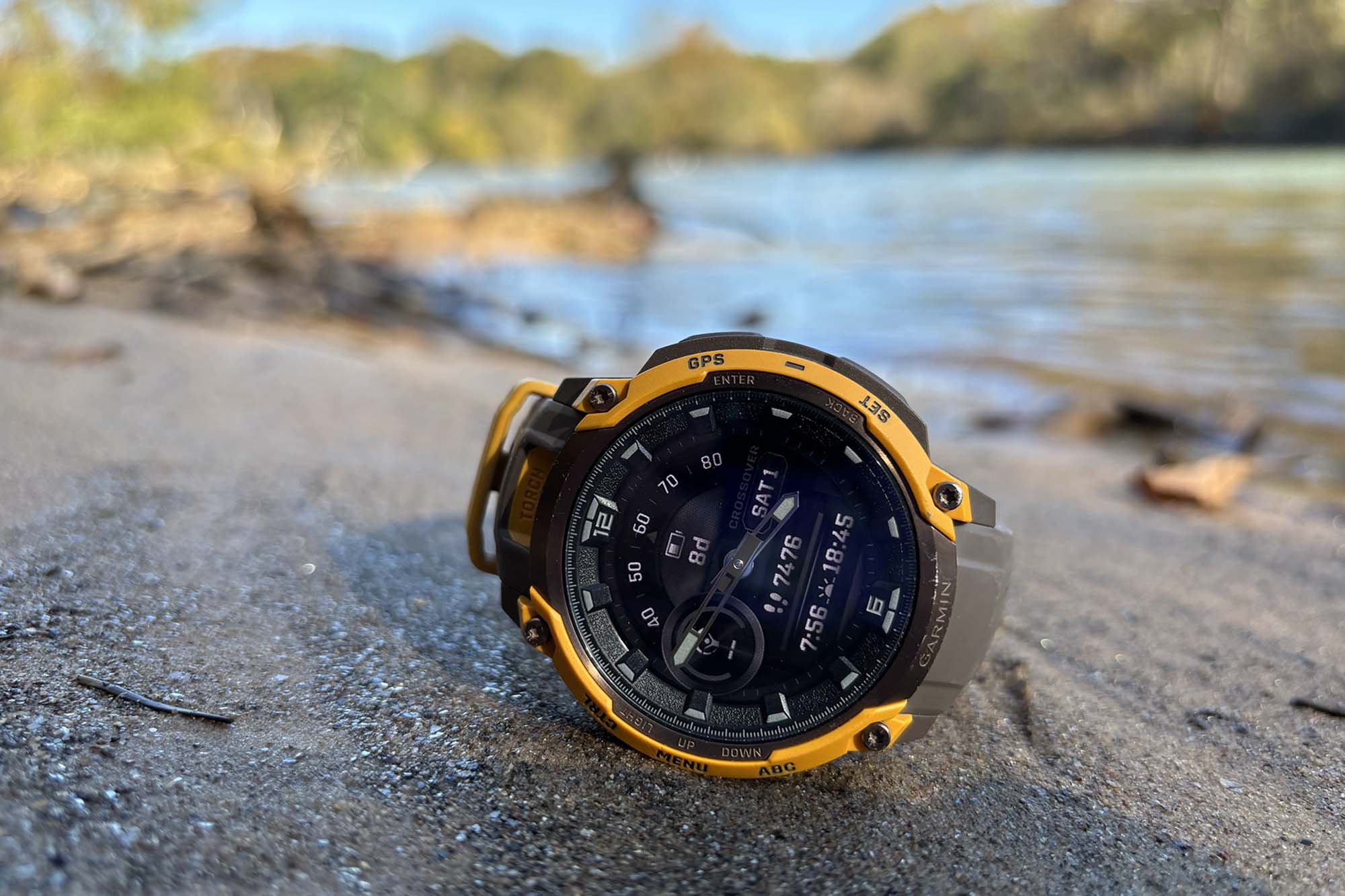 The Garmin Instinct Crossover AMOLED worn on a wrist in a wooded outdoor setting.