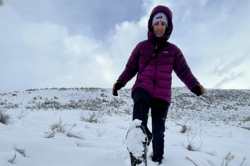 A hiker trekking through a vast, white winter landscape wearing winter gear.