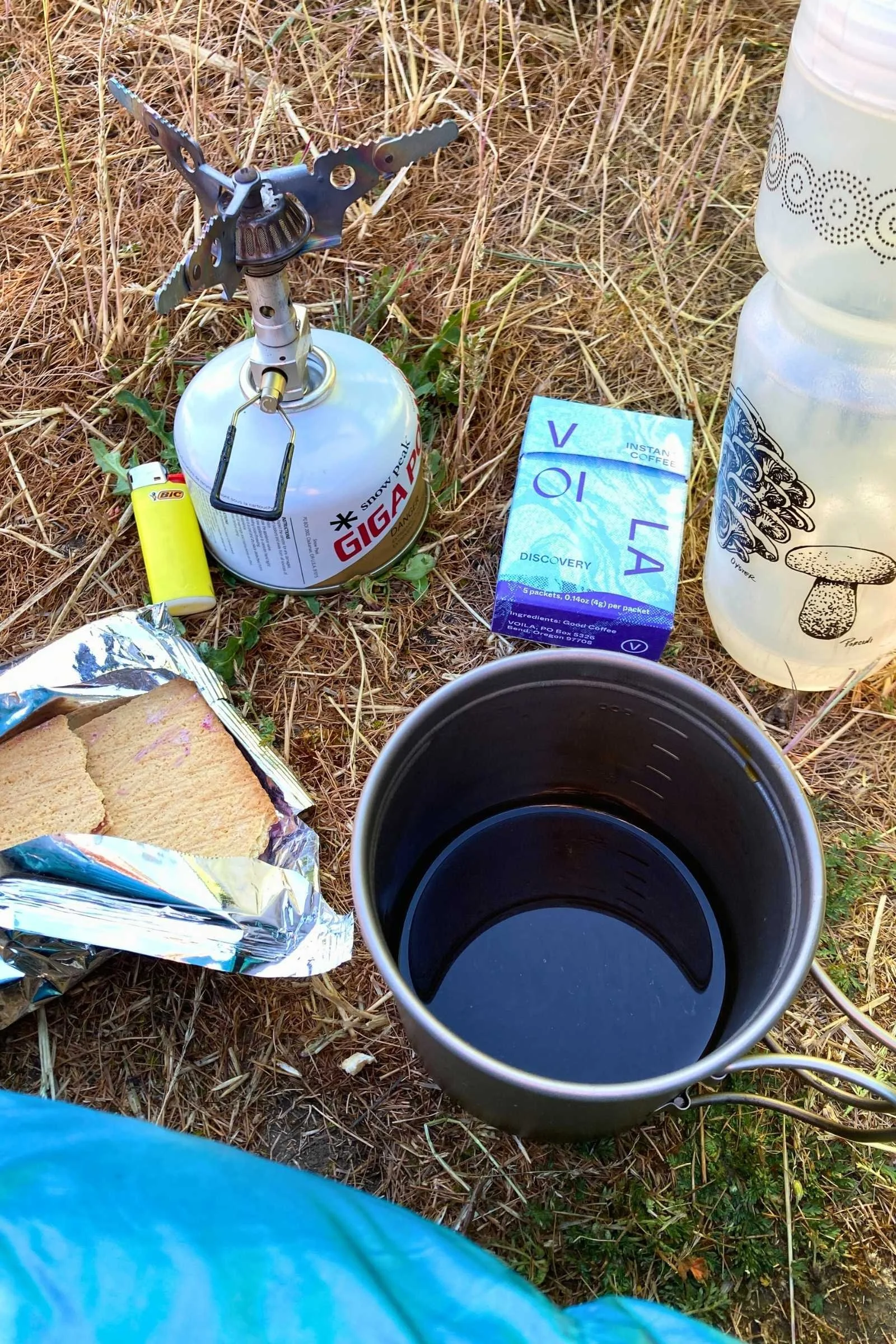 A hand pouring hot water into a camping mug with coffee instructions visible nearby.