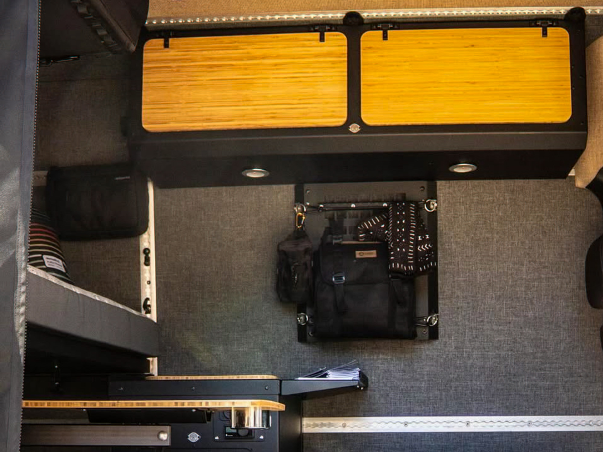 Campervan interior showing bed platform, cabinets, and a table attached to modular steel tracks.