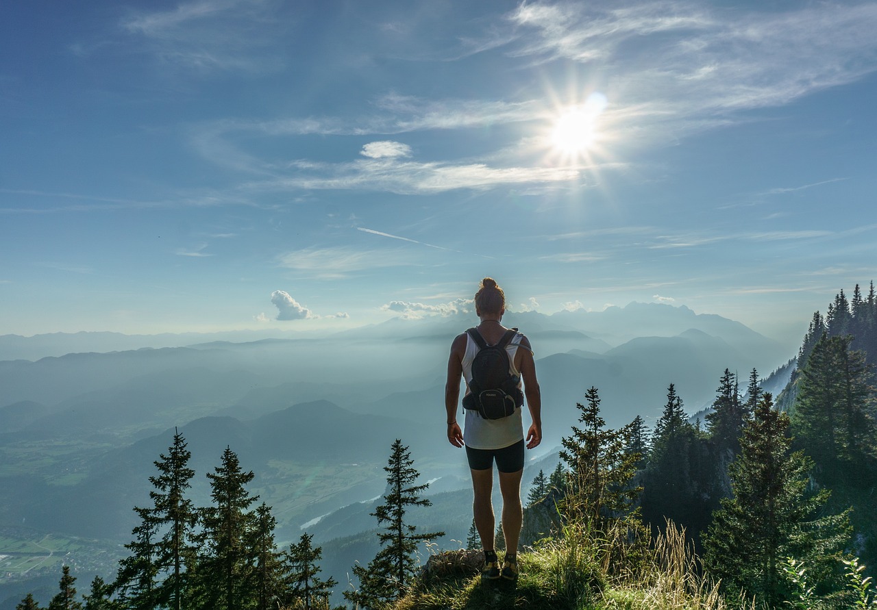 A hiker wearing a grey soft-sided cooler backpack walking along a scenic forest trail