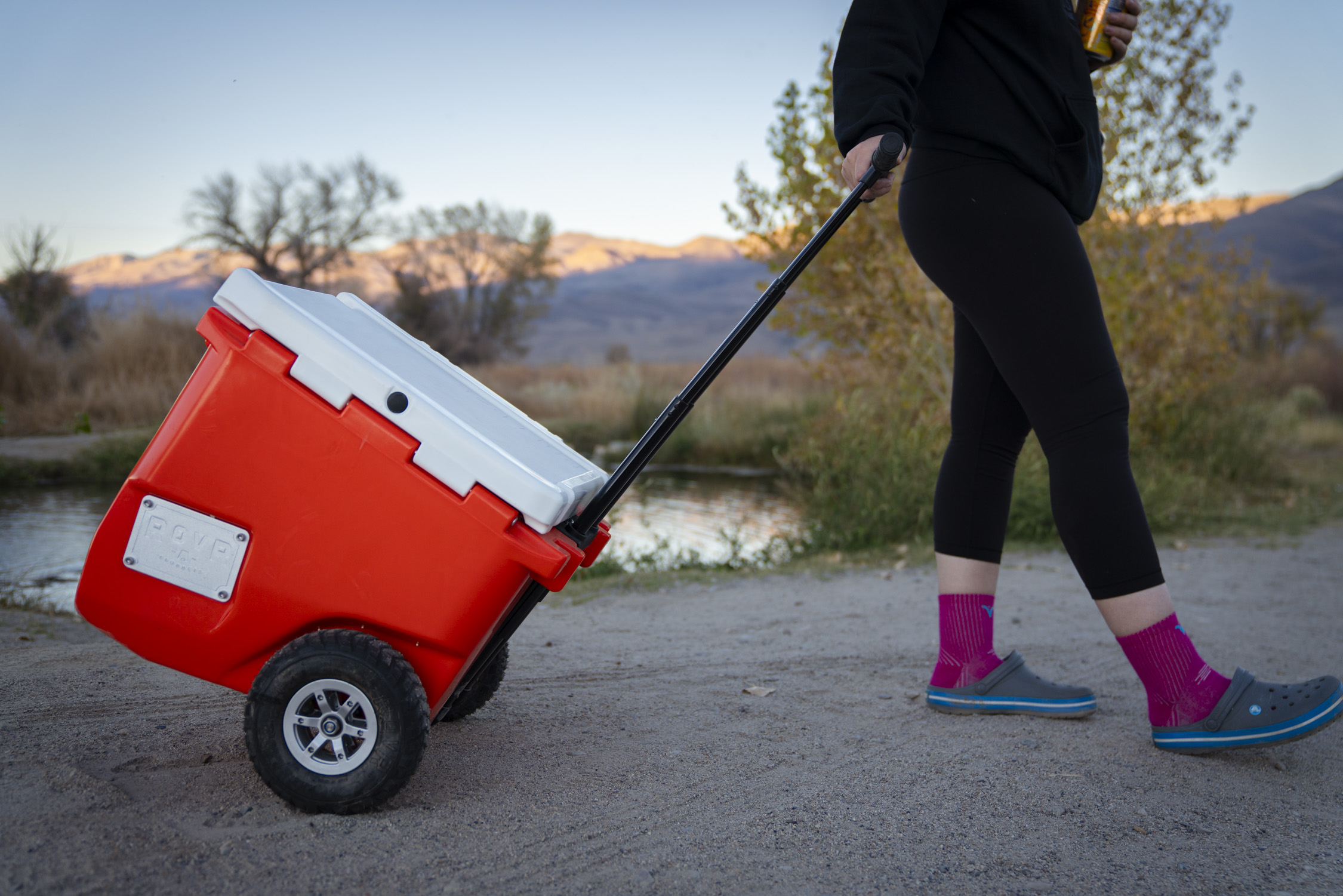 A colorful RovR cooler with large all-terrain wheels being moved on a path.