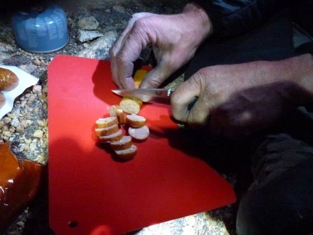A close-up of a high-quality folding knife being used for food preparation on a camping trip.