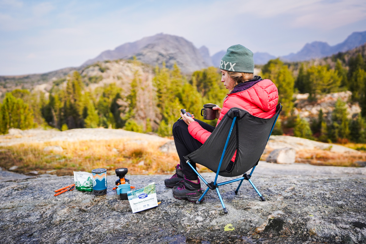 A woman sitting in a forest clearing using a handheld Garmin satellite messenger.