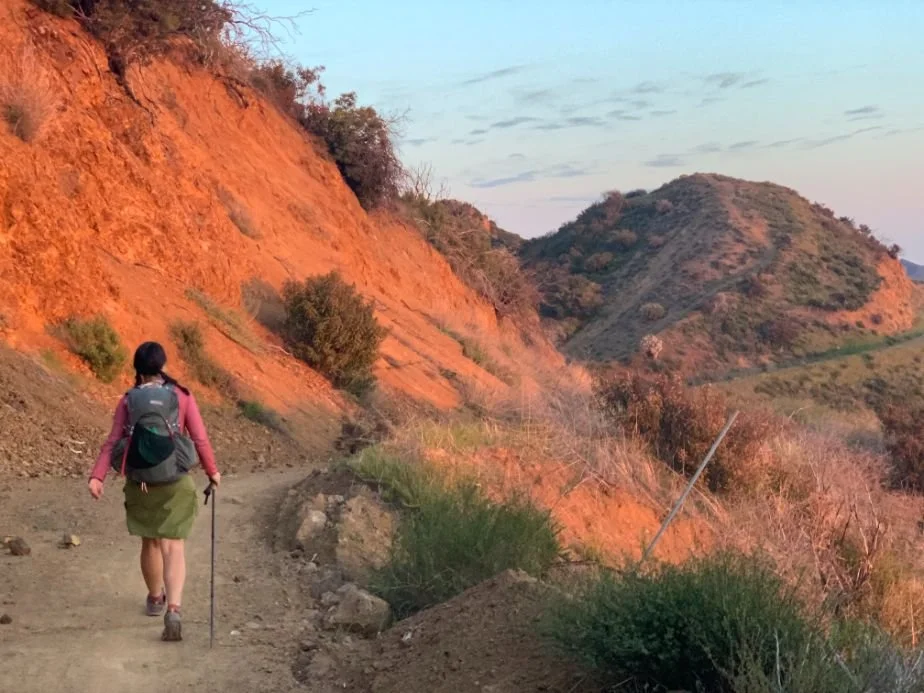 A mountainous trail overlooking the Pacific Ocean during a golden hour sunset.