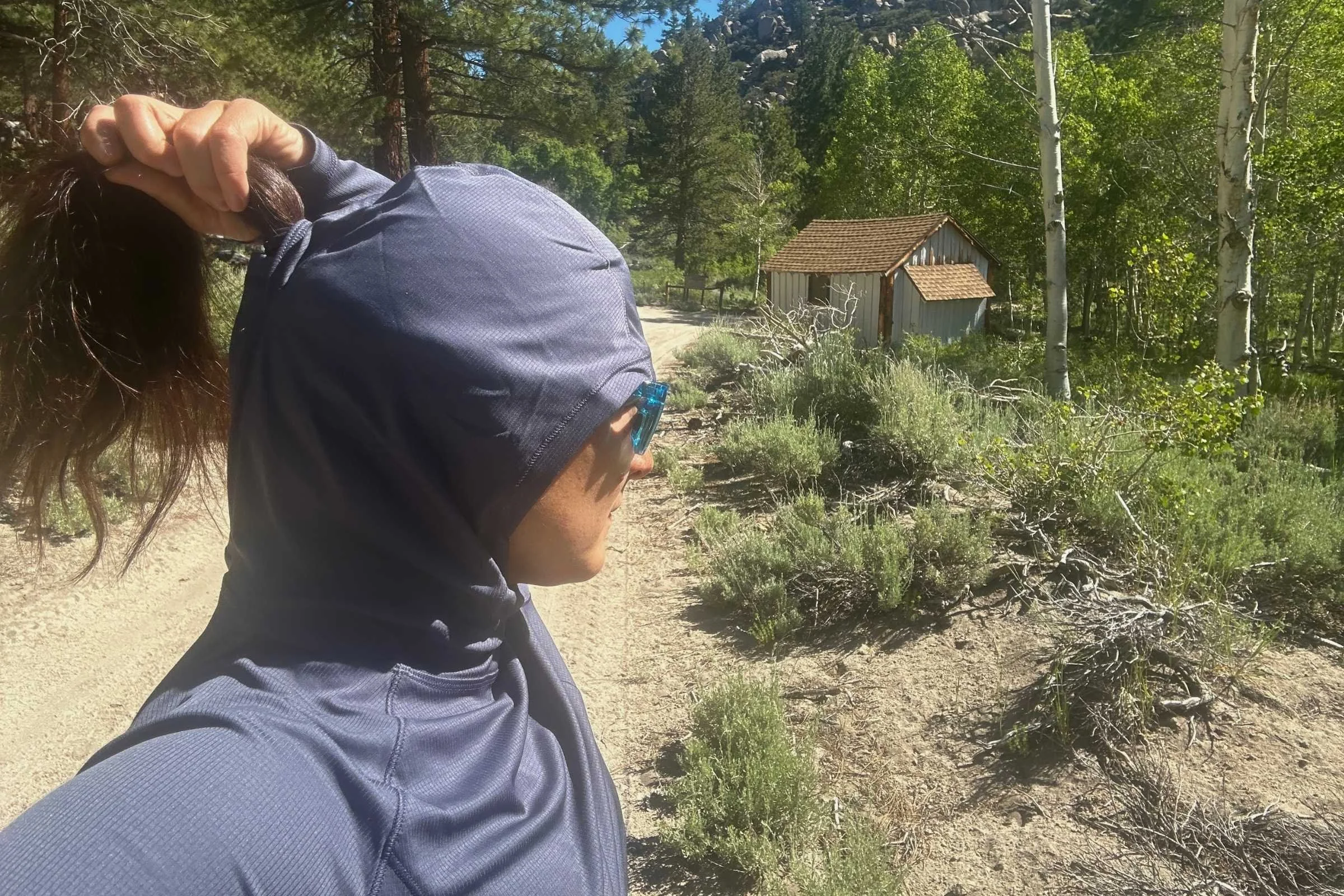 Rear view of the REI Flash Shade hoodie showing a person with their ponytail threaded through the hood opening.