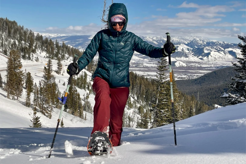 A hiker wearing KEEN Revel IV boots climbing a steep, snow-covered mountain slope.