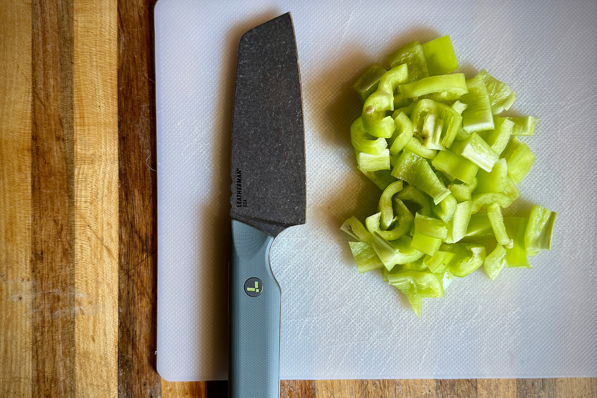 Leatherman Rustle knife on a white cutting board next to sliced green peppers.