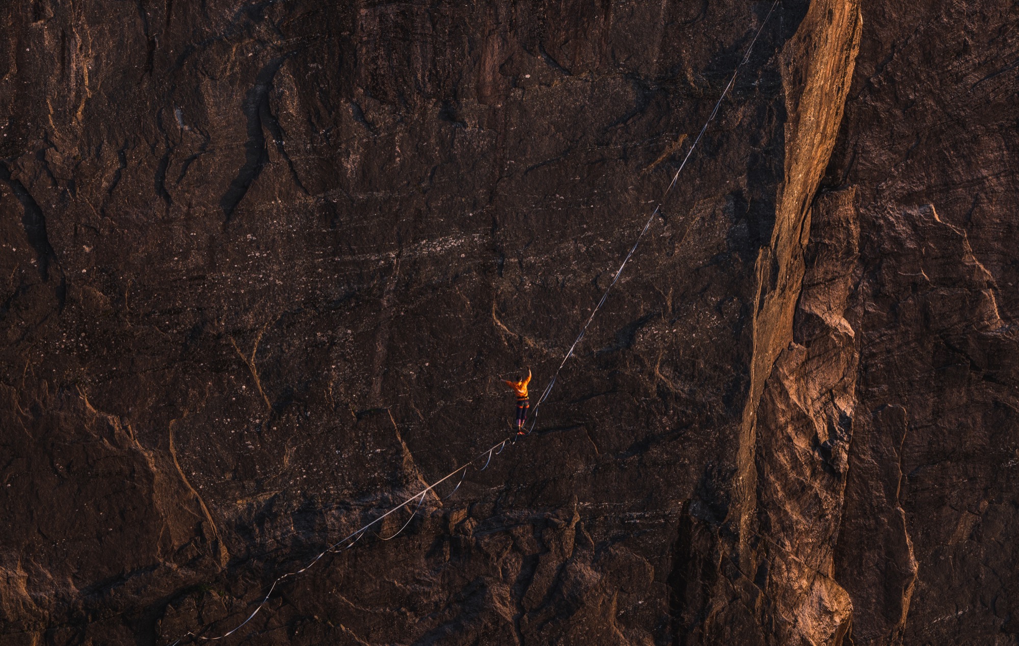 A slackline rigger crossing high-altitude webbing between rock faces.