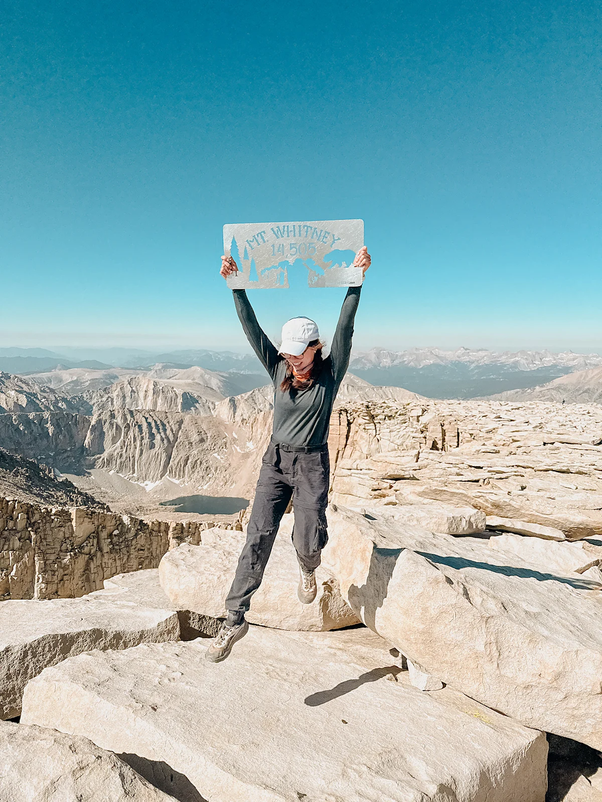 A hiker standing on the rocky summit of Whitney wearing trail runners.
