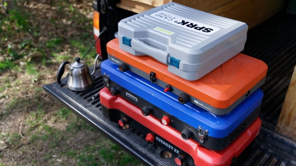 Side-by-side comparison of a large two-burner camping stove and a compact backpacking stove on a wooden surface.