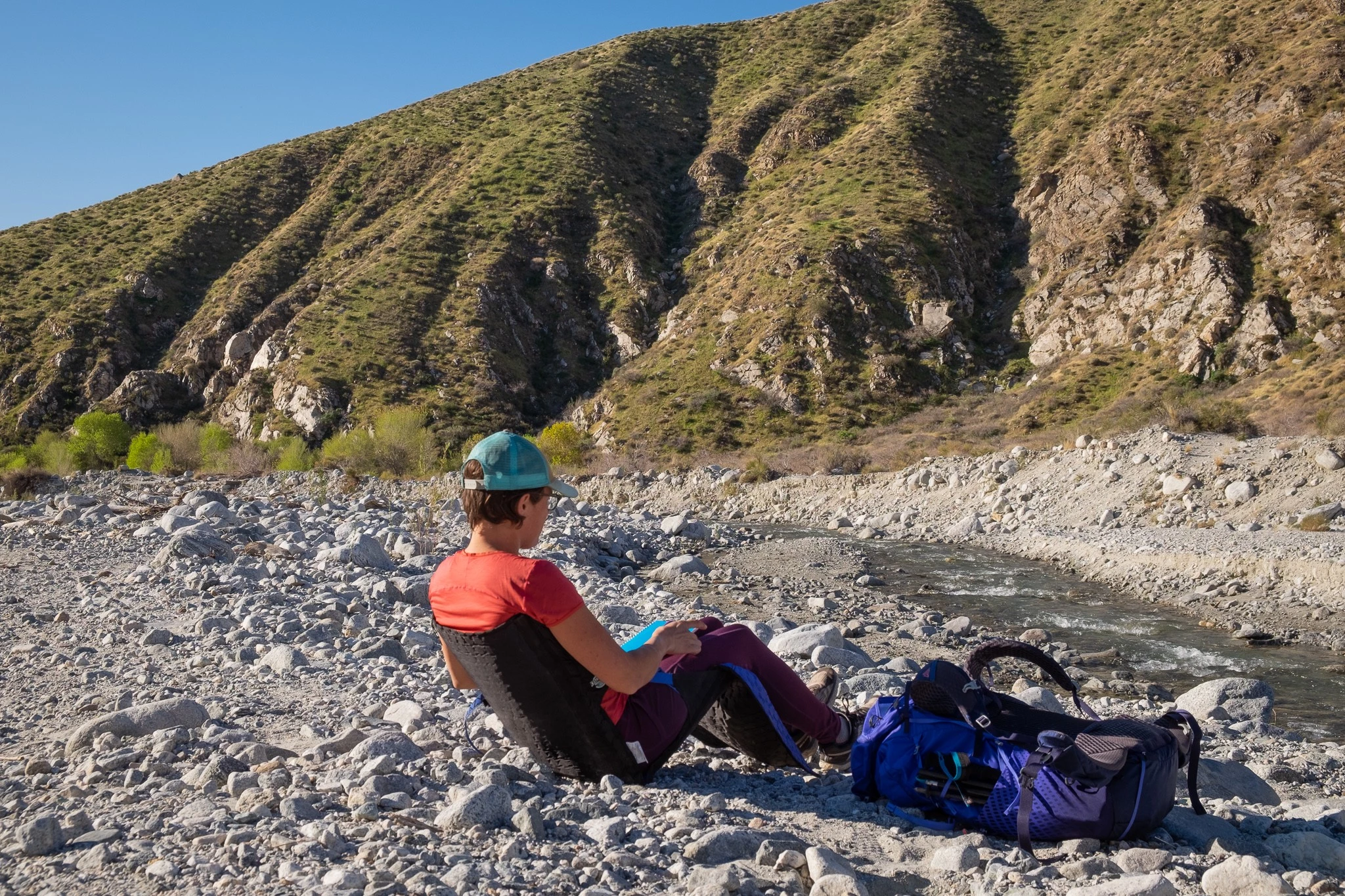 A hiker using a legless foam chair on the forest floor during a break.