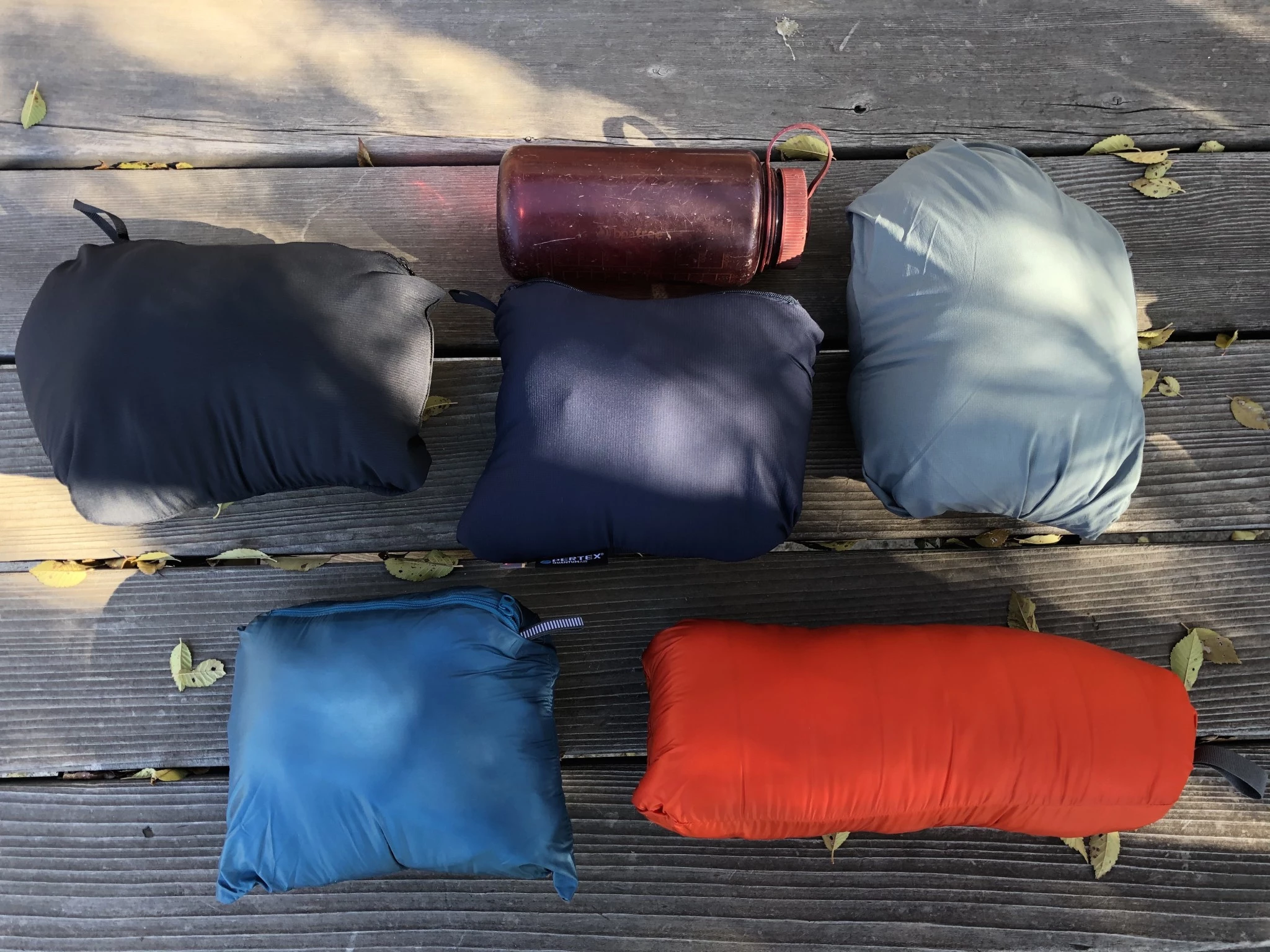 Several insulated jackets stuffed into their own internal pockets next to a water bottle for scale.