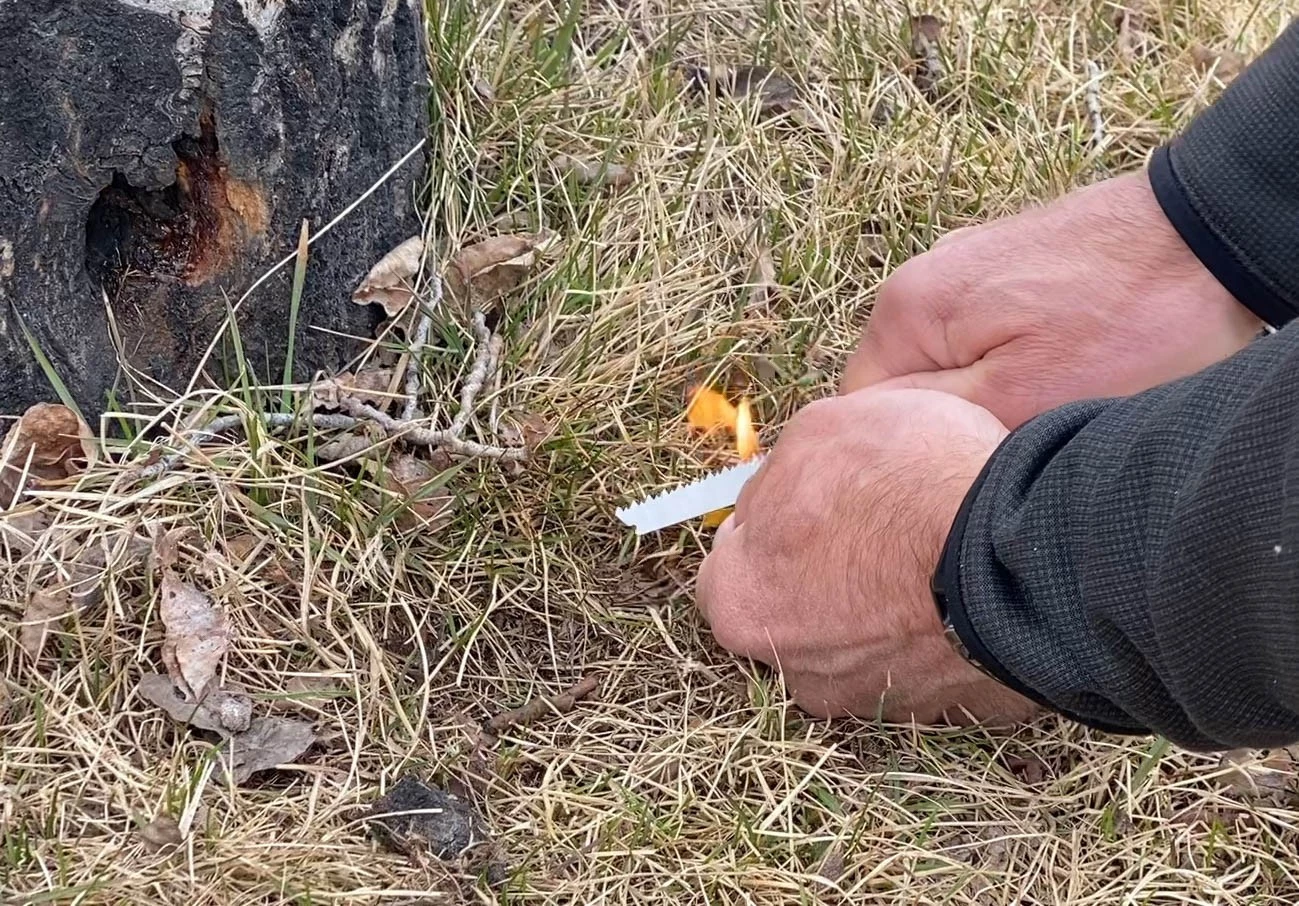 A small campfire being started using the ferro rod and survival components of a multi-tool.