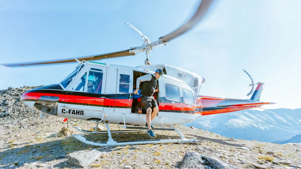 A group of trail runners near a helicopter on a remote mountain peak.