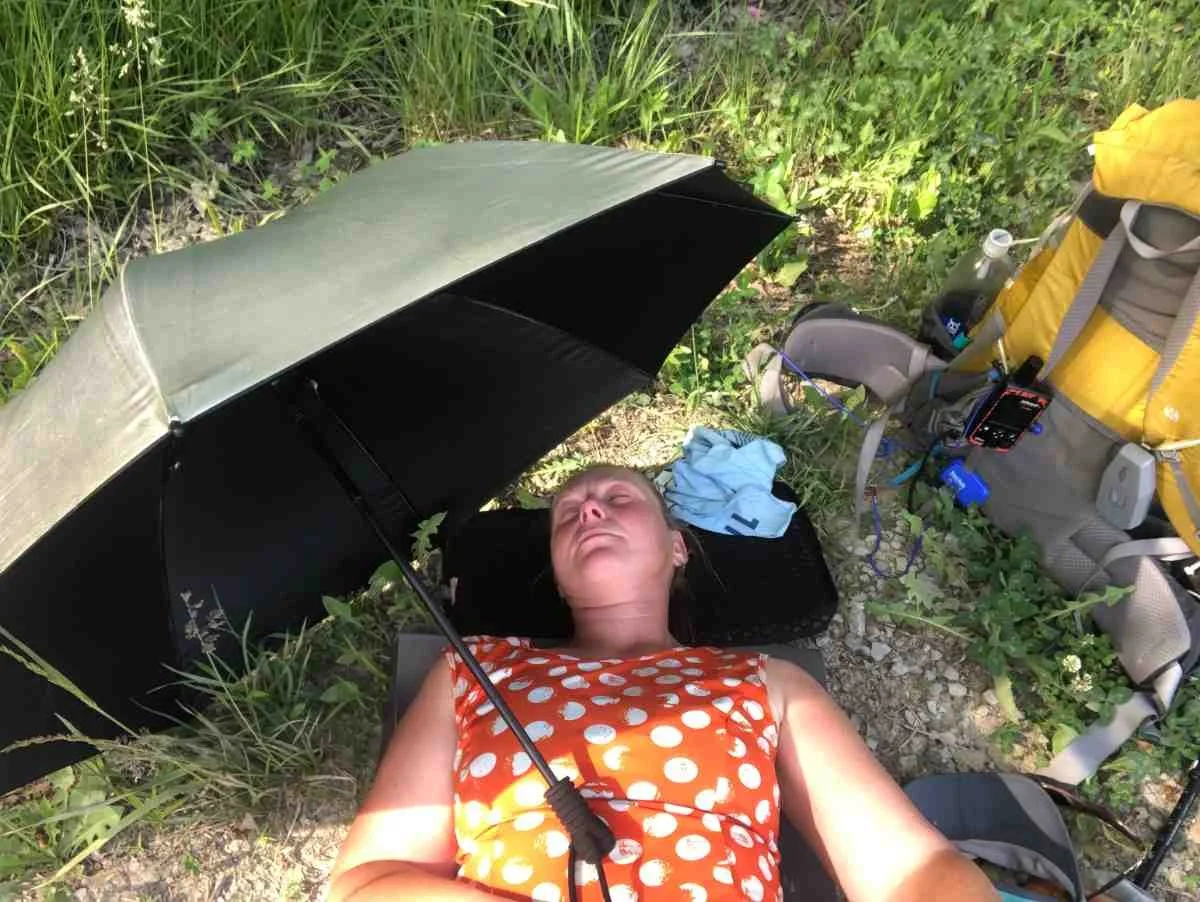 A hiker taking a break under the shade of a silver trekking umbrella.
