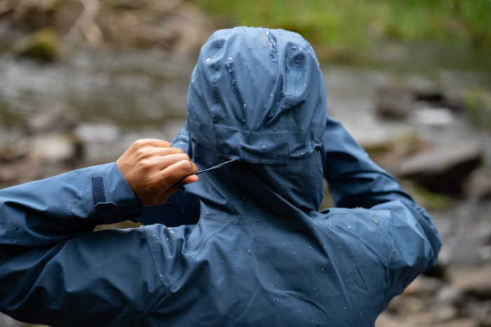 Close-up of a hand adjusting the drawcord on a rain jacket hood.