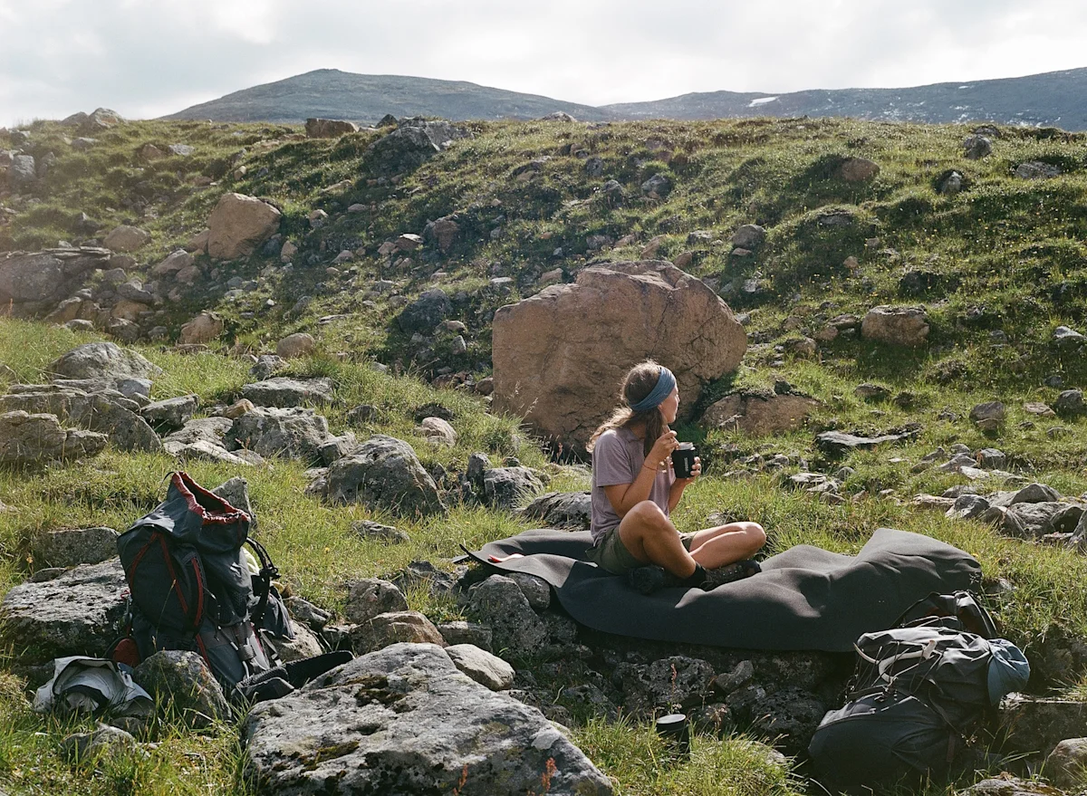 Two hikers sitting on a rock in the Swedish mountains drinking coffee.