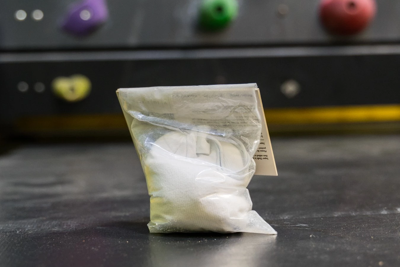 A hand squeezing a white refillable chalk ball inside a chalk bag.