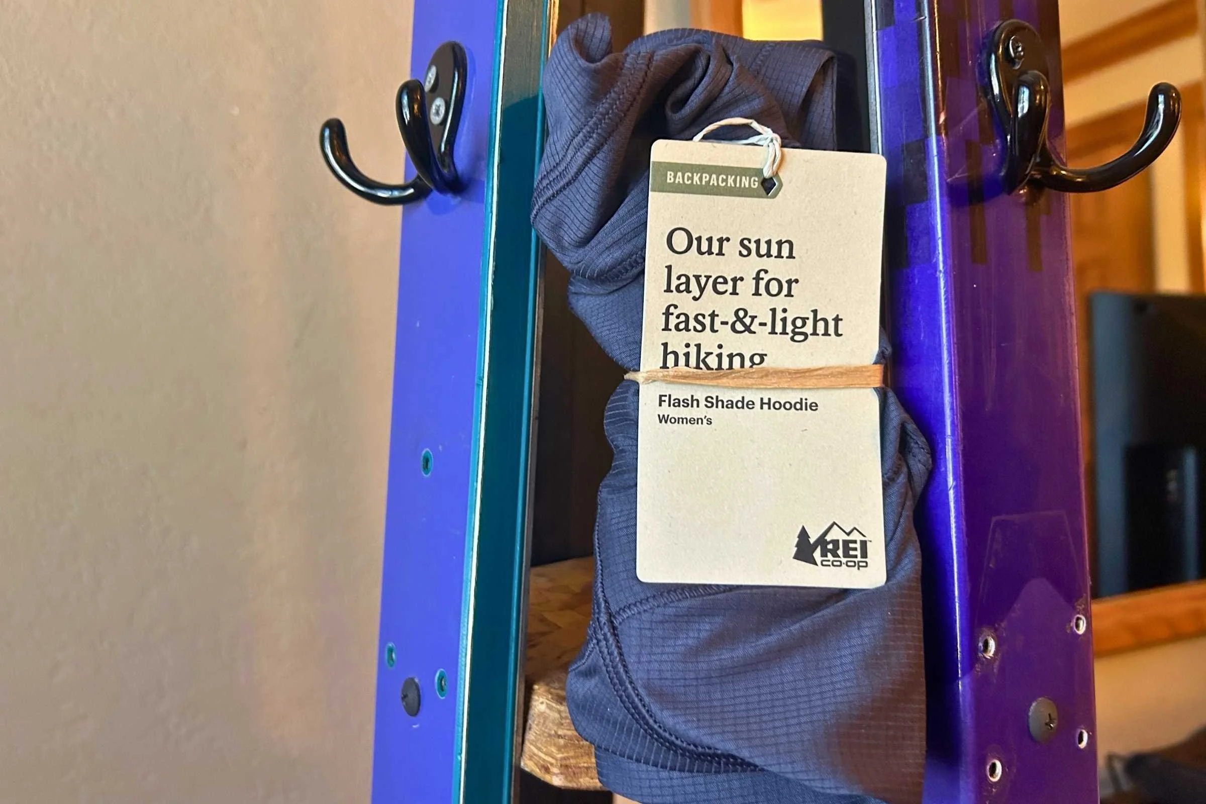 REI Flash Shade hoodie packaged in a simple recyclable cardboard tag with no plastic wrapping.