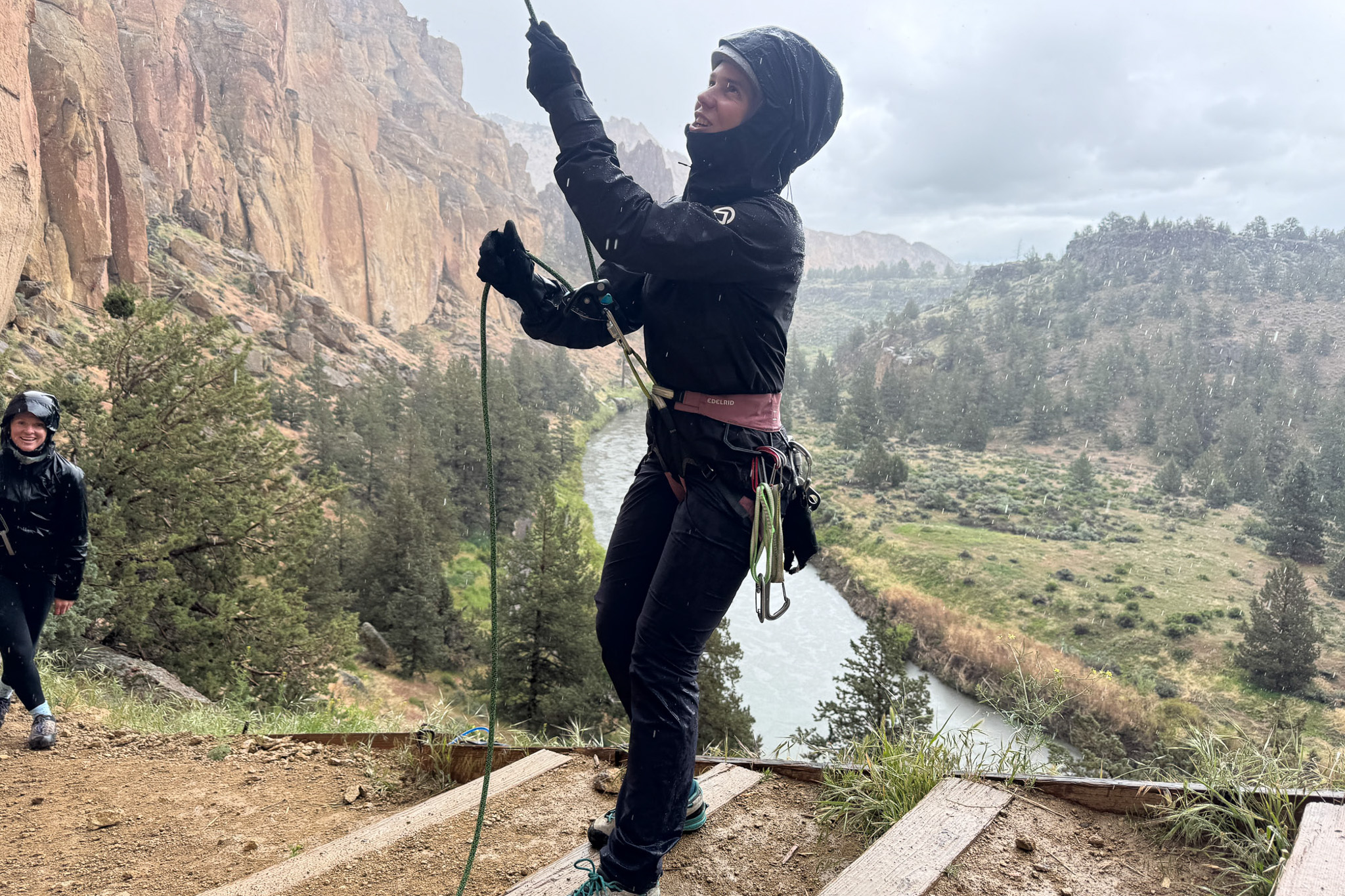 A woman belays a climber at Smith Rock State Park while wearing a technical rain shell.