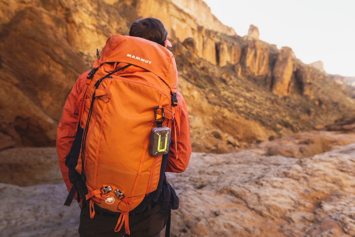 The orange Zoleo communicator clipped to the shoulder strap of a large backpack.
