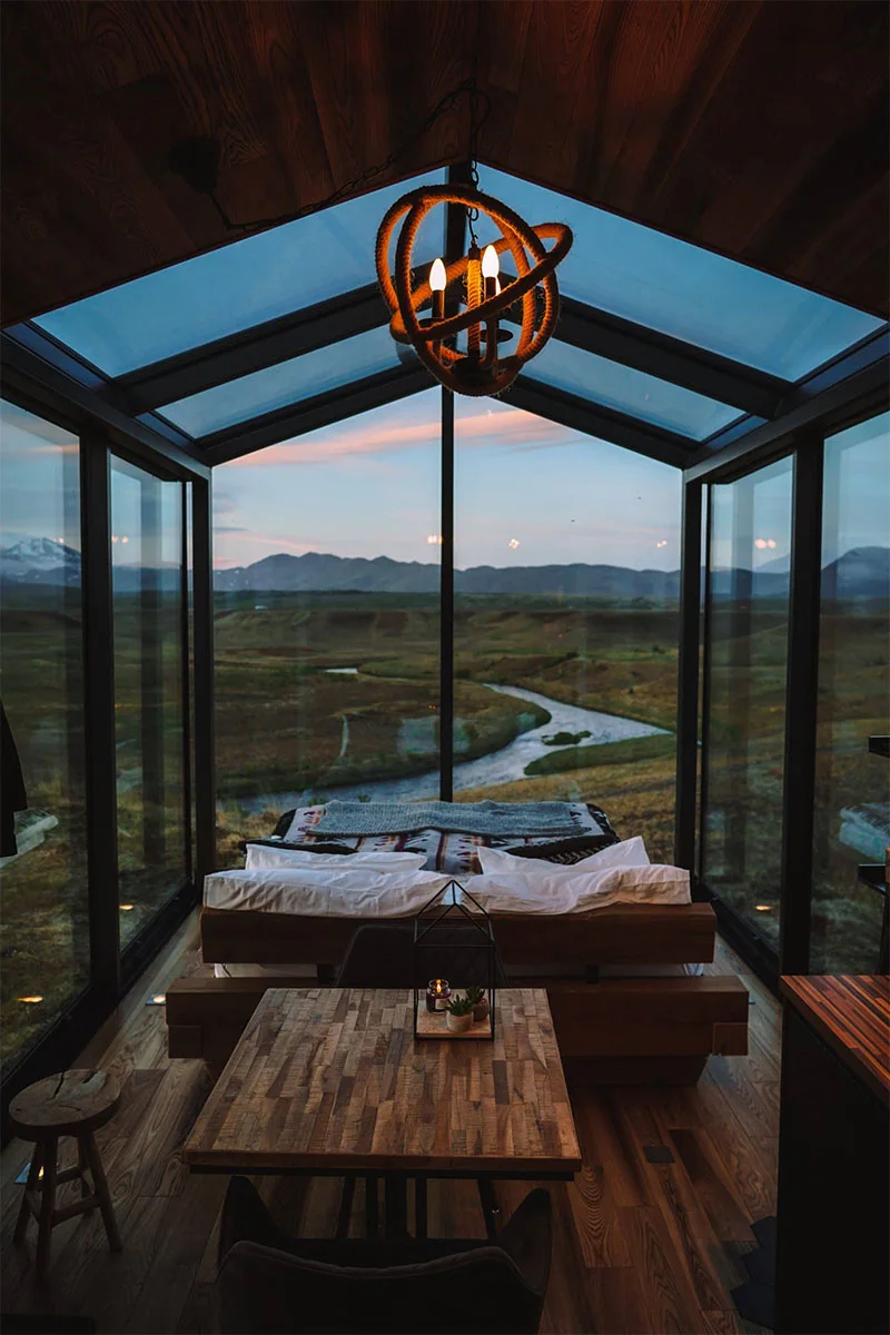 Interior view of a Panorama Glass Lodge featuring floor-to-ceiling windows overlooking a desolate landscape.
