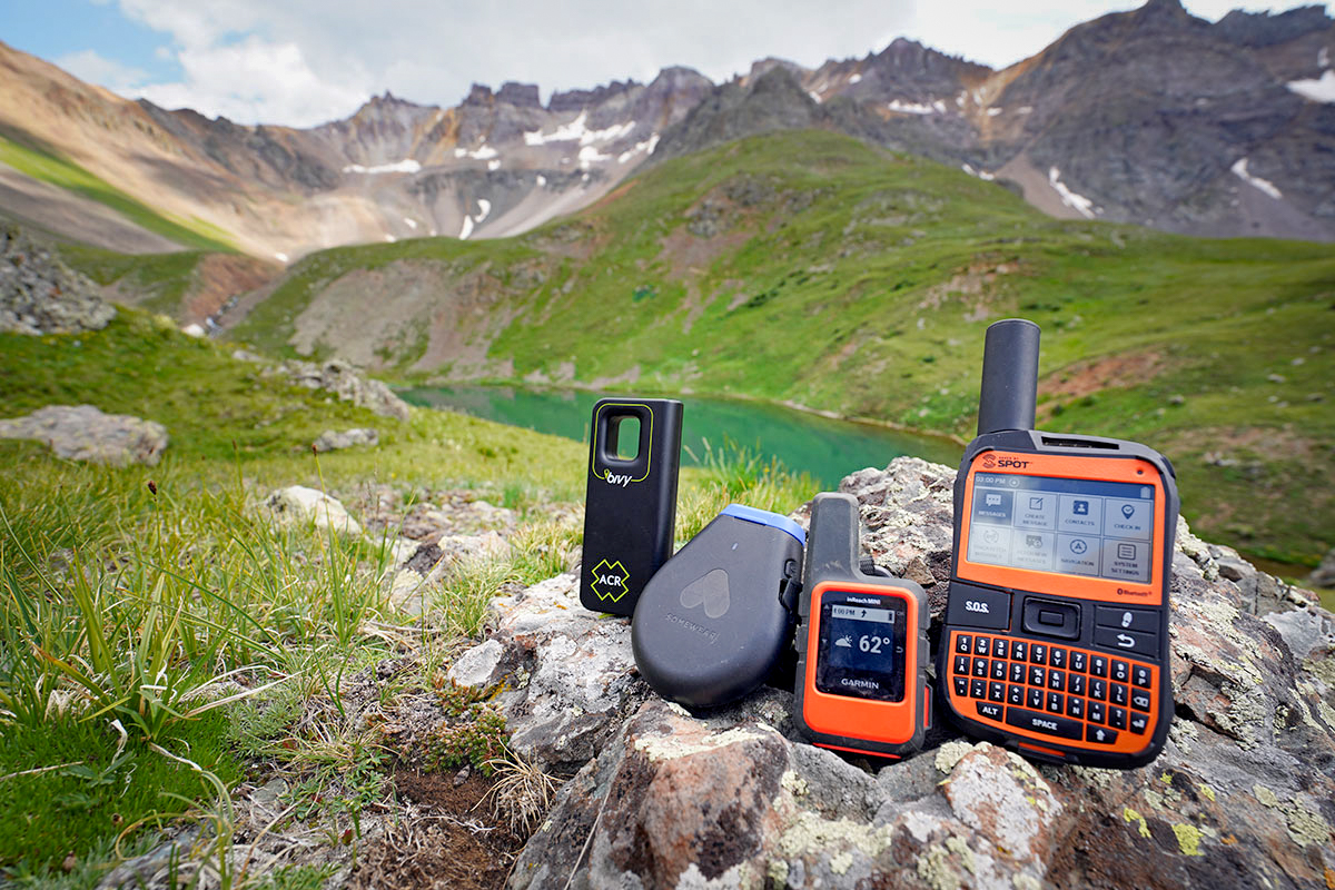 The Bivy Stick, Somewear Global Hotspot, Garmin inReach Mini, and SPOT X laid out on a rock in the mountains.