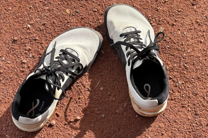A pair of ivory Notace Yama T1 shoes resting on dry red dirt alongside hiking gear.
