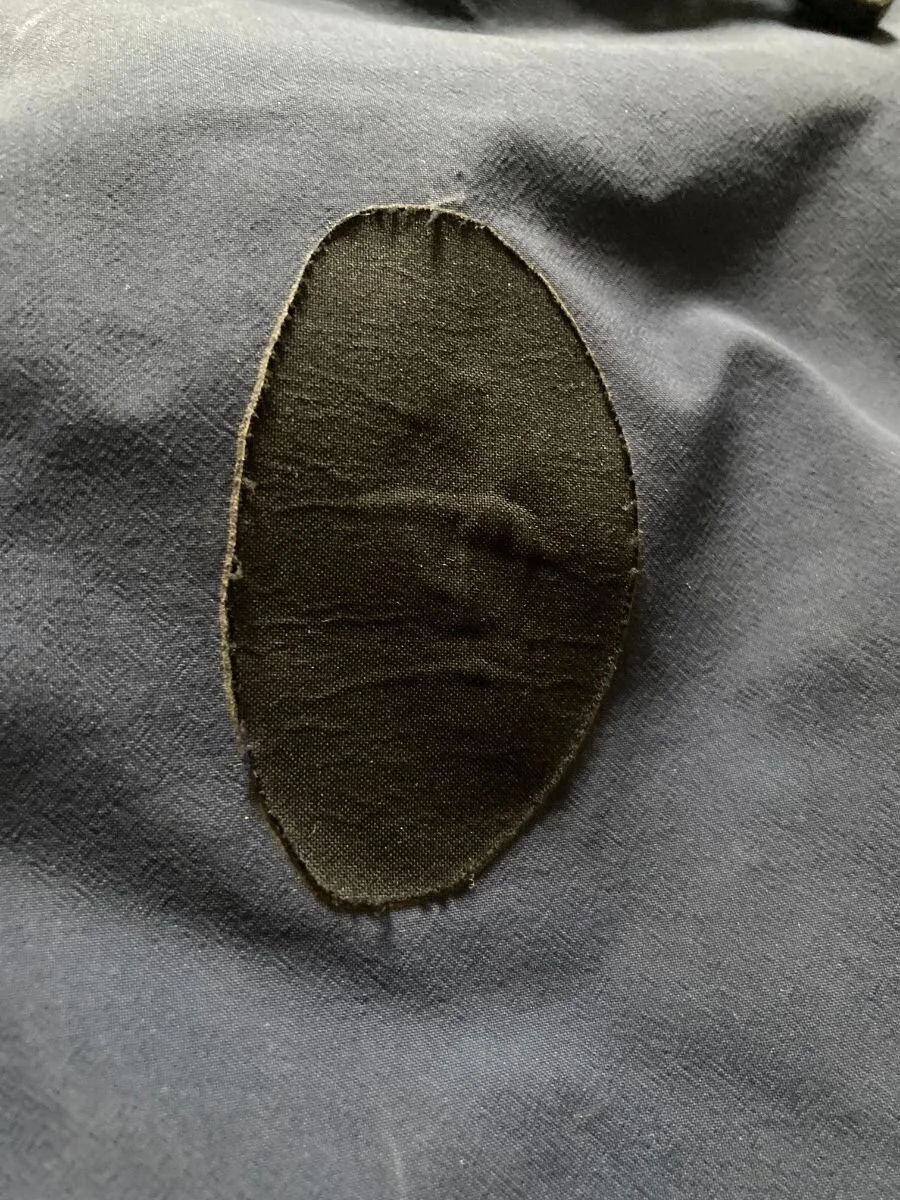 A pair of scissors trimming a repair patch for a technical jacket into a rounded shape.