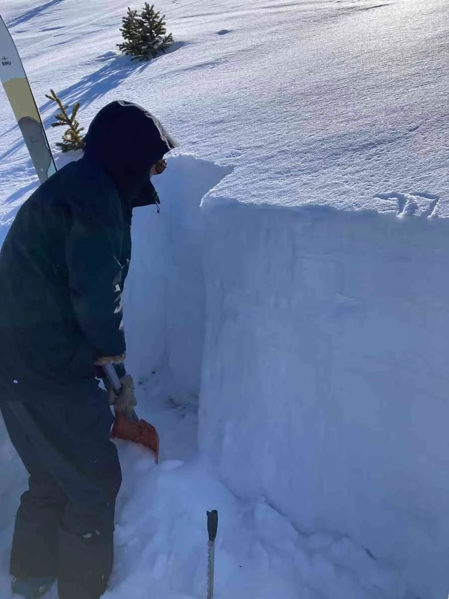 A person using a metal avalanche shovel to excavate a snow pit for snowpack analysis.