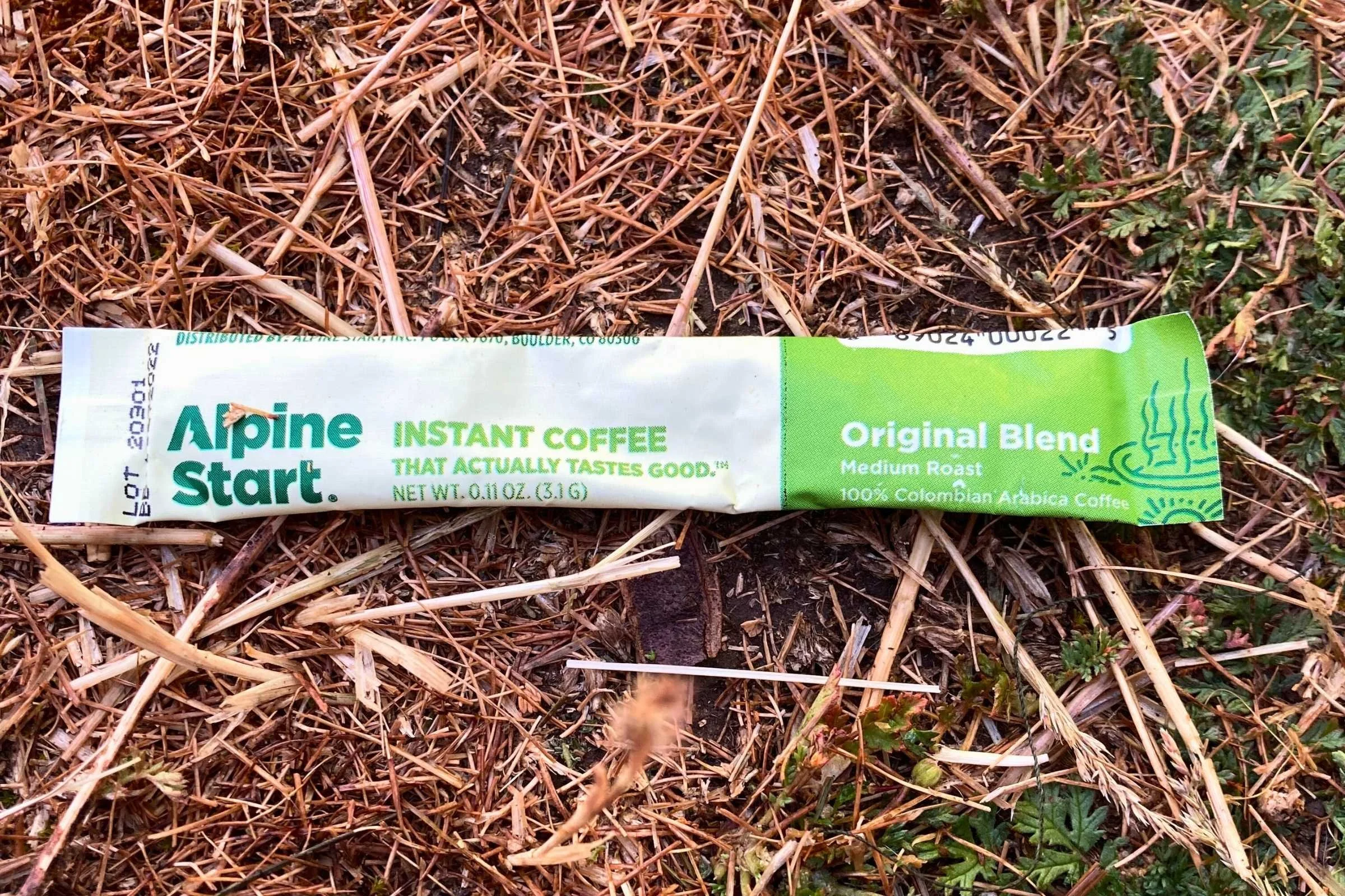 Individual sachets of Alpine Start Original Blend coffee next to a titanium camping mug.