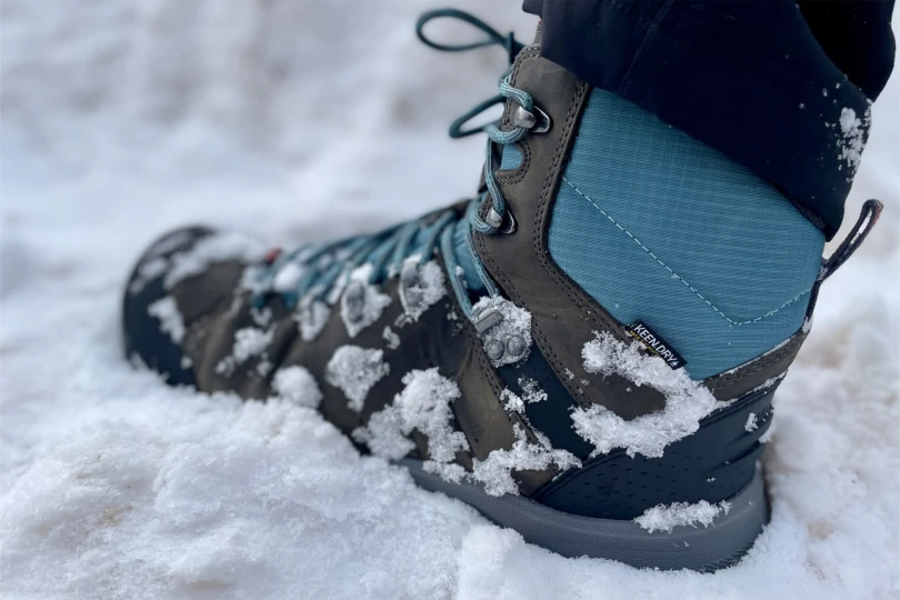 A KEEN Revel IV boot submerged in soft snow showing the waterproof breathable membrane tag.