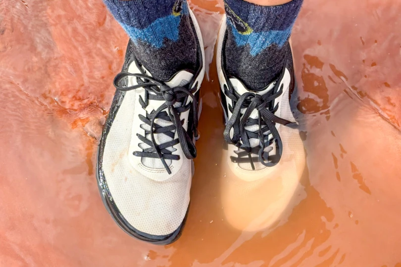 The Notace Yama T1 submerged in shallow water on a muddy hiking trail.