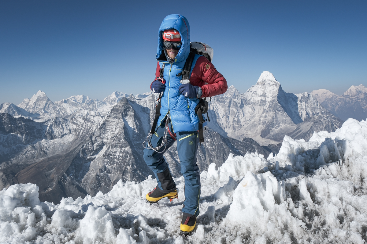 A mountaineer on a steep, snowy ridge in Nepal carrying technical climbing gear.