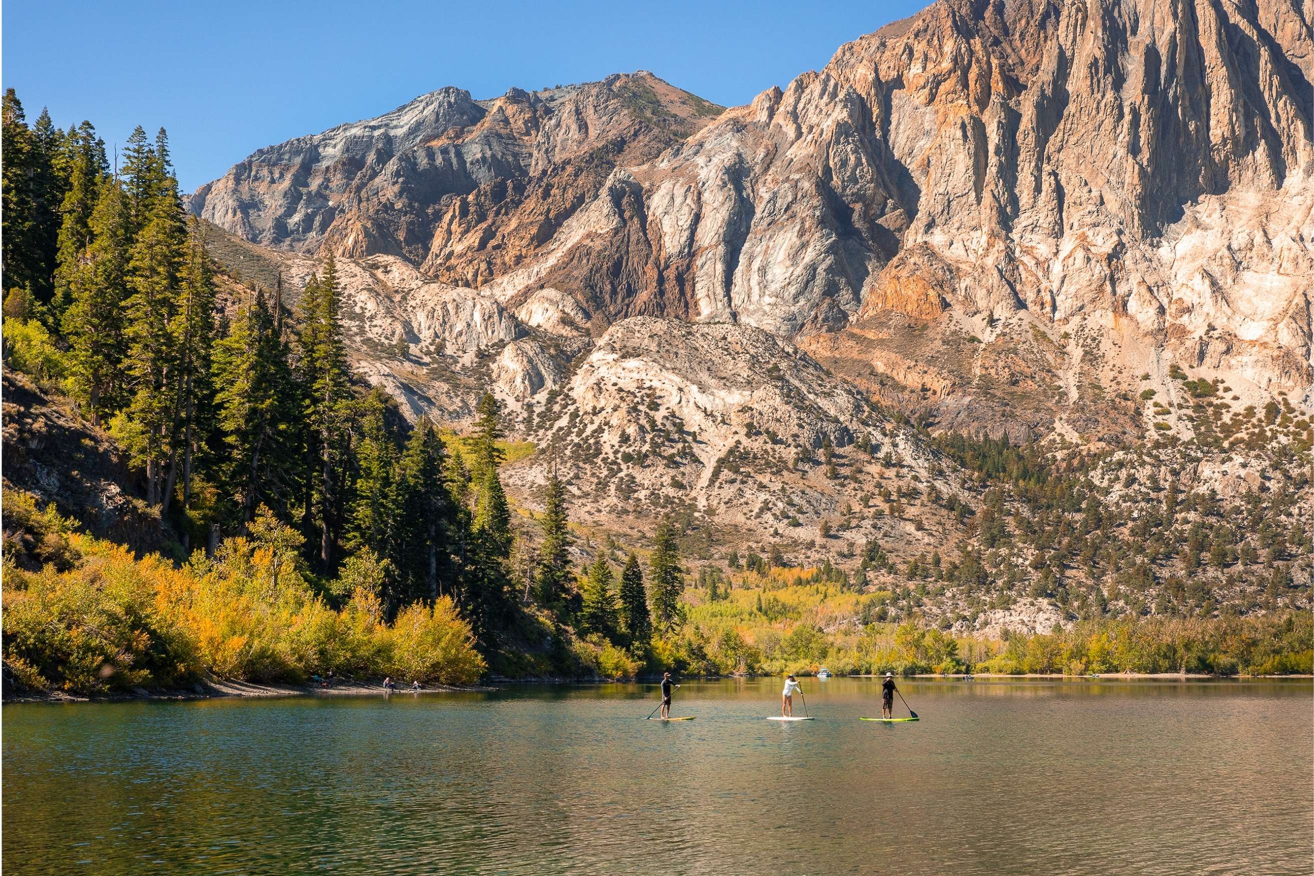 Crystal clear blue lake reflecting rugged grey mountains and golden autumn trees on its surface.