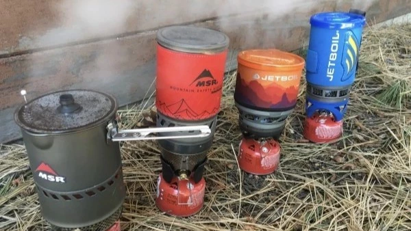 A small backpacking stove being used to prepare pour-over coffee outdoors.