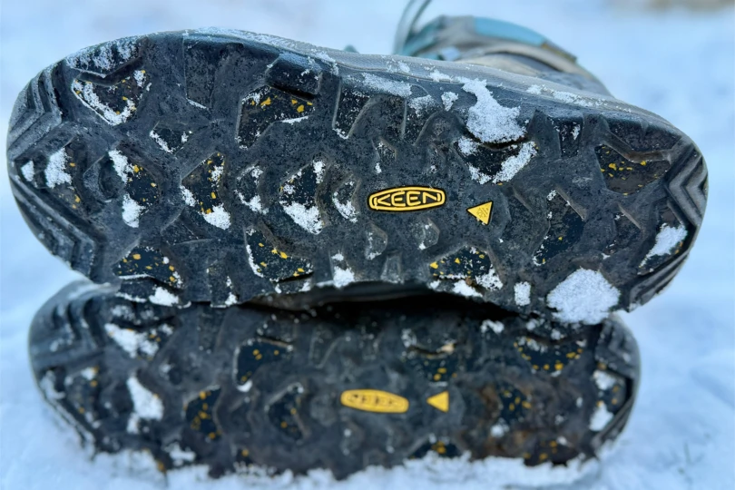The bottom outsole of a KEEN boot showing deep lugs and traction details with snow.