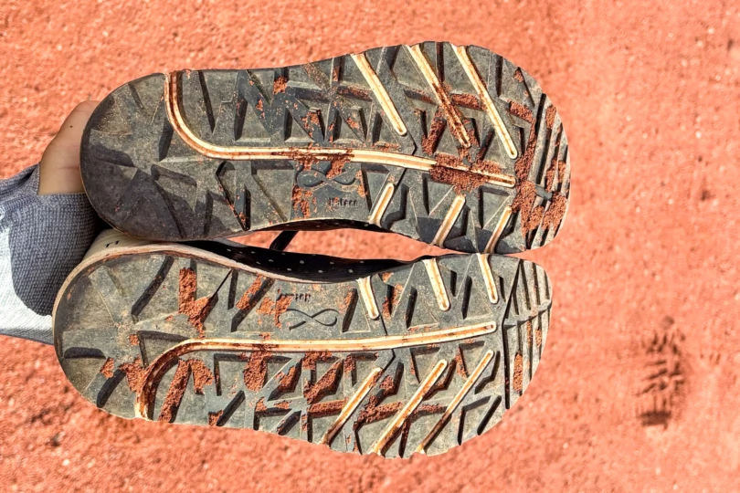 Bottom view of the Notace Yama T1 outsole showing triangular lugs covered in red dust.
