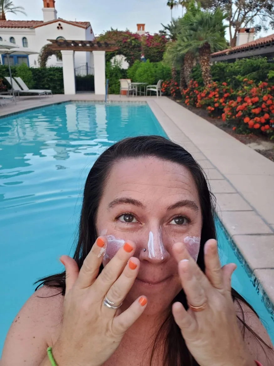 The author blending a mineral sunscreen onto her face while sitting by a pool.