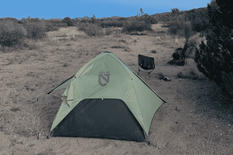 A small backpacking tent set up in a sandy dry wash surrounded by desert hills.